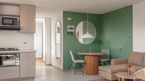 A modern kitchen with a microwave, oven, and built-in cabinets. There is a dining area with a round table and chairs, and a sofa in the living room. - NOK Stylish Studio w Balcony in Laureles Medellin (Medellín)