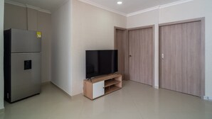 Una sala moderna con un televisor de pantalla plana sobre un mueble de madera, un refrigerador empotrado y dos armarios de madera.