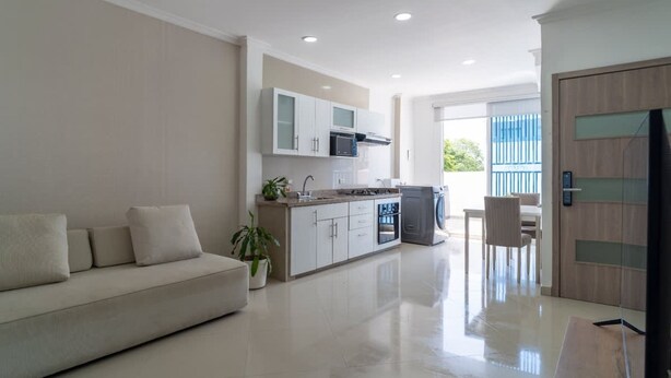 Una sala moderna con un sofá, una zona de cocina con armarios y electrodomésticos, y un comedor con una mesa y sillas.