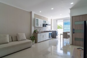 Een moderne woonkamer met een bank, een keuken met kasten en apparatuur, en een eethoek met een tafel en stoelen.