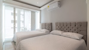Habitación de hotel con dos camas, un ventanal grande y un equipo de aire acondicionado.