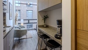 Una cocina moderna con armarios de madera, una cafetera y una pequeña zona de estar con taburetes.
