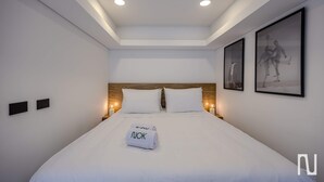 Una habitación de hotel moderna con una cama bien hecha, iluminación empotrada en el techo y obras de arte en las paredes.