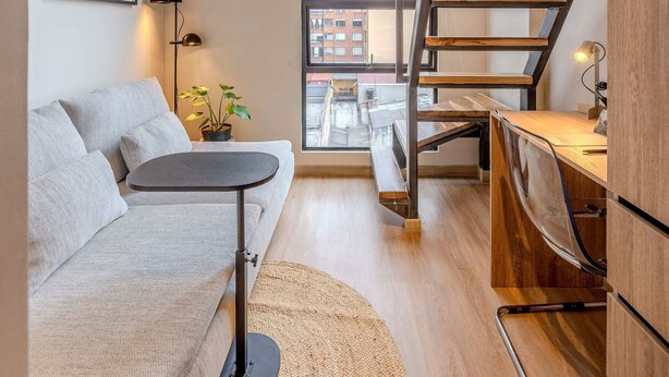 En moderne lejlighed med sofa, et lille bord, en trappe og udsigt over byen.