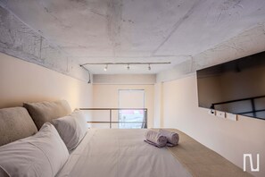 A bedroom with a bed, pillows, a rolled-up towel, a TV on the wall, and a window with a view. - NOK Luxury Studio in Chapinero (Bogotá)