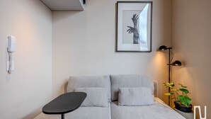 Et moderne værelse med en grå sofa, et lille sort bord, et indrammet kunstværk, en gulvlampe og en potteplante.