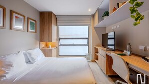 Una camera d'albergo moderna con un letto, una scrivania, una TV e ampie finestre.