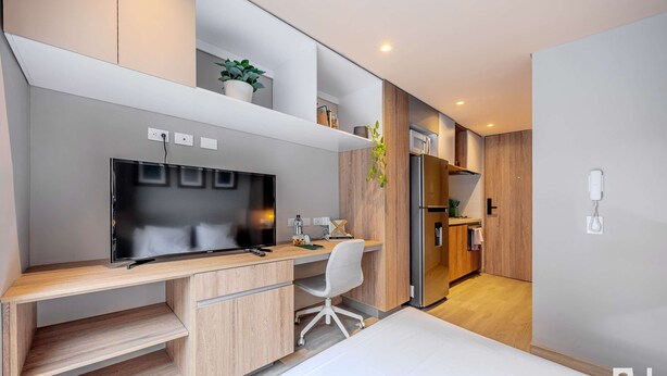 Camera moderna con un letto, una scrivania con un computer, una TV e un angolo cottura con microonde e frigorifero.