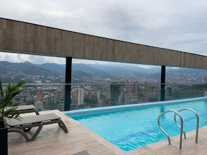 A modern rooftop pool with clear glass walls, offering a panoramic city view with mountains in the background. - NOK Beautiful 2BR Apartment in El Poblado (Medellín)