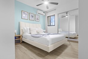 A modern bedroom with a large bed, a ceiling fan, and a window with a view. - NOK Designer 2BR Loft Jardines 3 Punta Cana (Punta Cana)