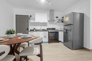 A modern kitchen with a stainless steel refrigerator, a built-in oven, and a microwave. There is a dining table with chairs and a potted plant. - NOK Designer 2BR Loft Jardines 3 Punta Cana (Punta Cana)