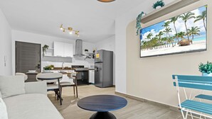 A modern living room with a sofa, a round table, and a TV displaying a beach scene. - NOK Designer 2BR Loft Jardines 3 Punta Cana (Punta Cana)