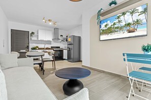 A modern living room with a sofa, a round table, and a TV displaying a beach scene. - NOK Designer 2BR Loft Jardines 3 Punta Cana (Punta Cana)