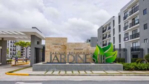 A residential complex entrance with a sign reading "JARDINESTUDIO" and a green abstract sculpture. - NOK Designer 2BR Loft Jardines 3 Punta Cana (Punta Cana)