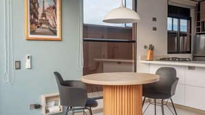 A modern kitchen with a round wooden table, two black chairs, a hanging pendant light, and a framed picture of the Eiffel Tower on the wall. - NOK Perfect 1BR in Laureles Medellin (Medellín)
