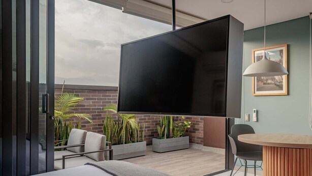 A modern hotel room with a large bed, a flat-screen TV mounted on the wall, a dining area with a round table, and potted plants. - NOK Perfect 1BR in Laureles Medellin (Medellín)