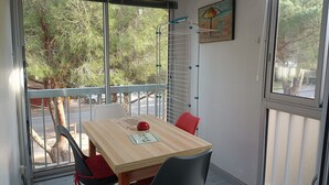 Una zona de menjador amb una taula de fusta, quatre cadires, un objecte vermell sobre la taula, i una finestra amb vista a arbres i un camí.