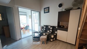 Un saló amb un sofà, una taula rodona petita i un armari. Hi ha una porta corredissa de vidre que dona a un balcó.