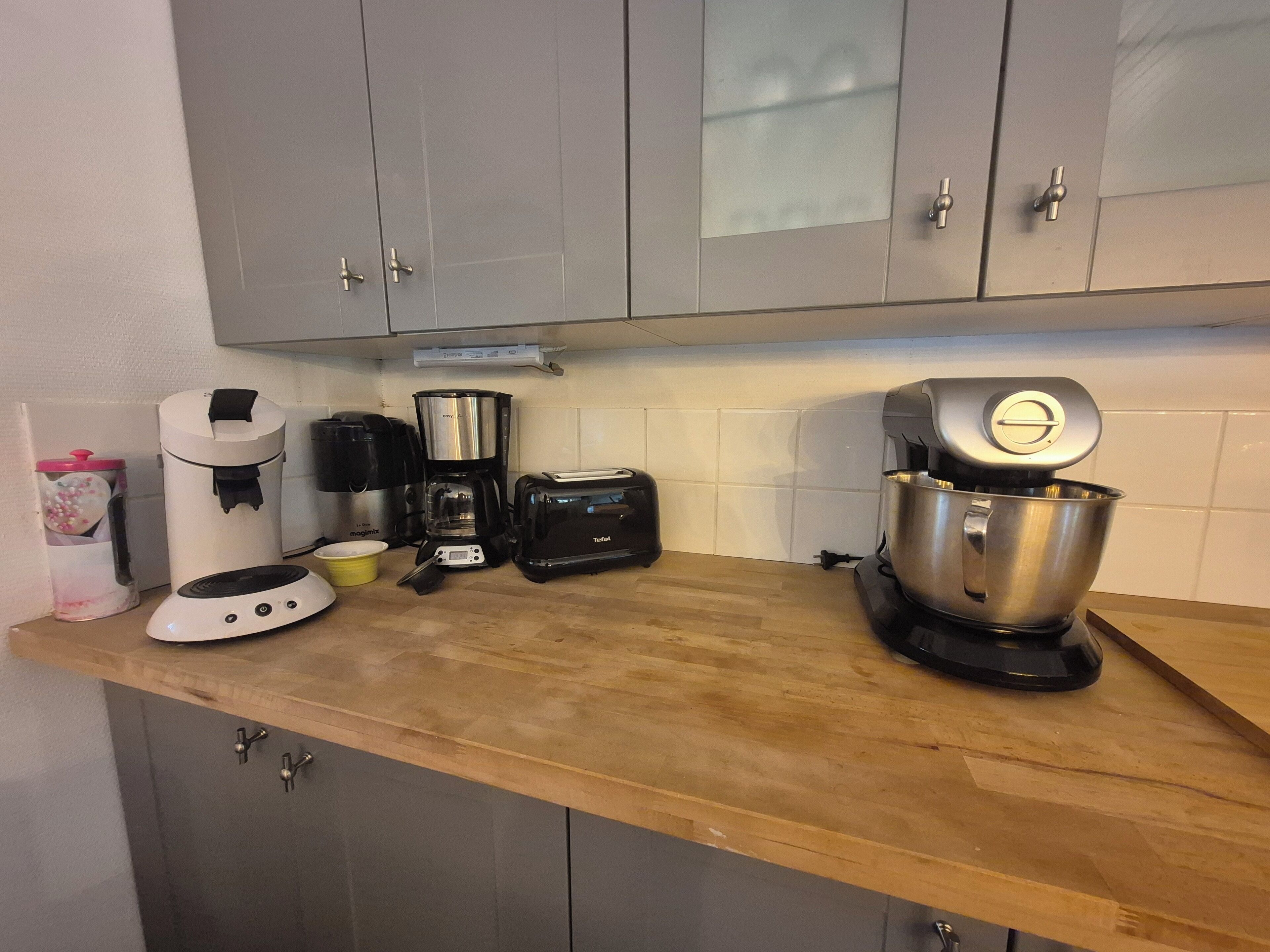 Una cocina con gabinetes grises, cafetera, tostadora y batidora.