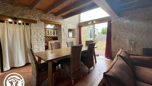 A rustic dining area with a wooden table and wicker chairs, a stone wall, and a view of the outside. - Renovated 3-bedroom cottage in Damvix with Wifi (Damvix)