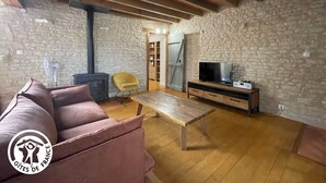 A cozy living room with a stone wall, wooden beams, a sofa, a TV, and a bookshelf. - Renovated 3-bedroom cottage in Damvix with Wifi (Damvix)