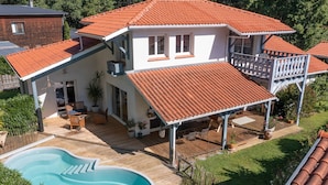 Ein zweistöckiges Haus mit Swimmingpool, überdachter Terrasse und umzäunter Terrasse.