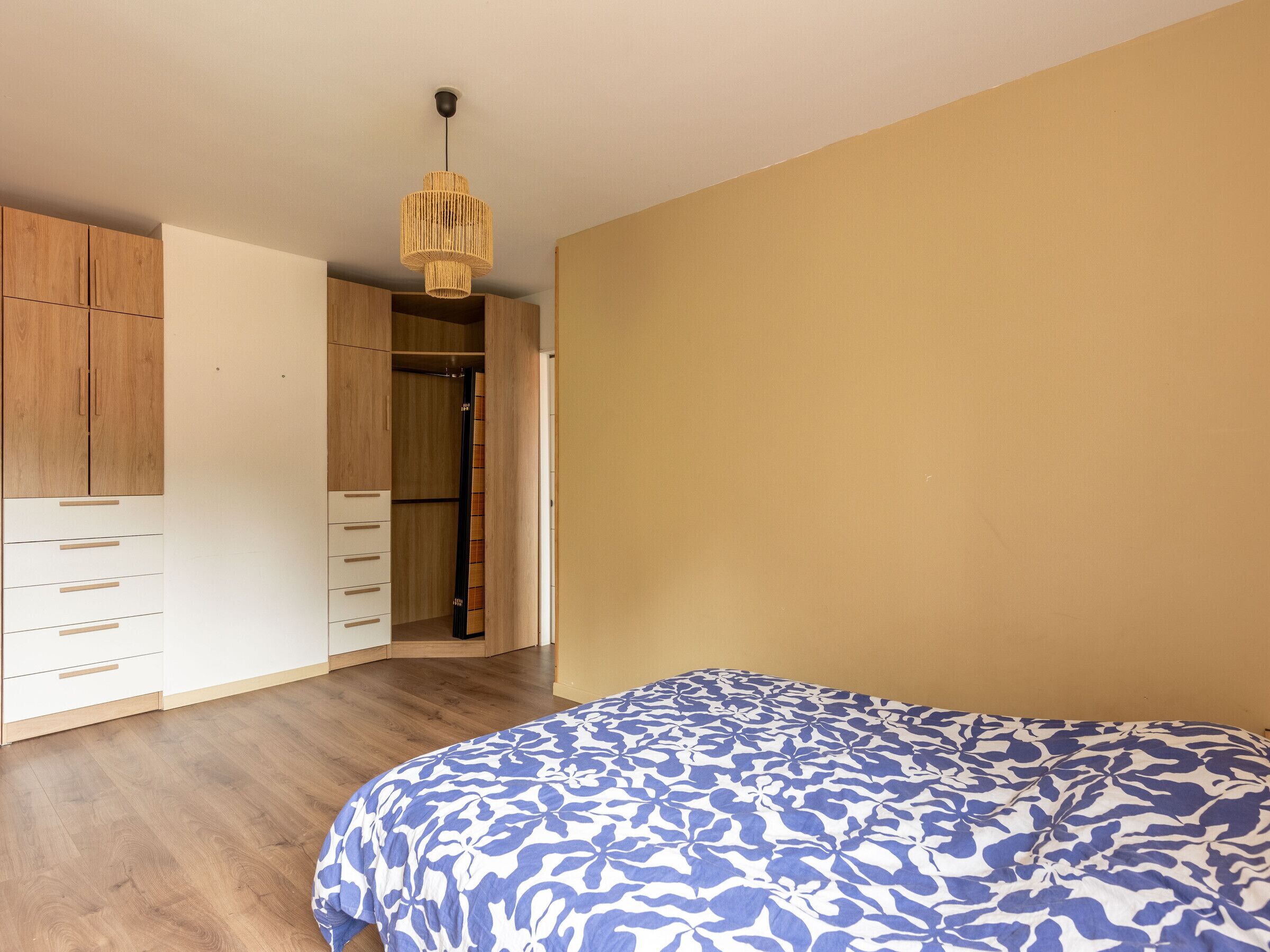 A bedroom with a bed, wooden wardrobe, and a hanging light fixture.