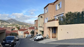 A residential street with houses, parked cars, and a mountain in the background. - Family house 4 rooms 8 people, near the beach in Banyuls-sur-Mer (Banyuls-sur-Mer)