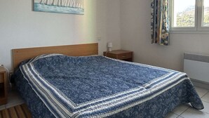 A bedroom with a bed, a nightstand, a lamp, a window with curtains, and a painting on the wall. - Family house 4 rooms 8 people, near the beach in Banyuls-sur-Mer (Banyuls-sur-Mer)