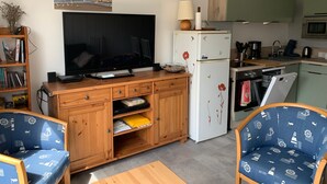 A compact living space with a TV, wooden furniture, a refrigerator, and a kitchen area. - Family home between beach and bay with private parking (Fort-Mahon-Plage)