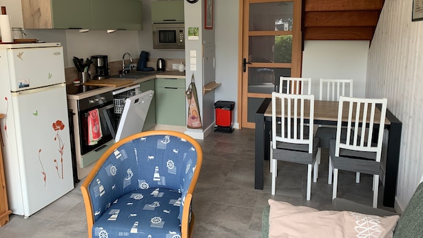 A compact kitchen with a microwave, oven, and dishwasher. There is a dining area with a table and chairs, and a small seating area with a patterned chair. - Family home between beach and bay with private parking (Fort-Mahon-Plage)