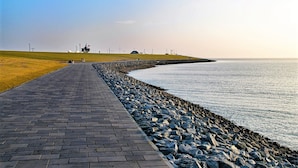 A paved walkway beside a rocky shoreline with a grassy area and distant structures. - “Apartment Föhr” in the heart of Büsum with balcony, centrally located and close (Büsum)