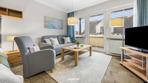 A modern living room with a grey sofa, a wooden coffee table, and a TV stand. There is a painting on the wall and a window with curtains. - “Apartment Föhr” in the heart of Büsum with balcony, centrally located and close (Büsum)