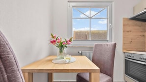 Une petite cuisine avec une fenêtre, une table ornée d’un vase de fleurs et une chaise.