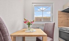 A small kitchen with a window, a table with a vase of flowers, and a chair. - “Apartment Amrum” in the heart of Büsum with balcony, centrally located and clos (Büsum)