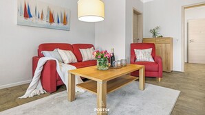 Un salon moderne avec un canapé rouge, une table basse en bois et un tableau représentant des voiliers accroché au mur.