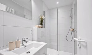 A modern bathroom with a white sink, toilet, and shower. - "Ferienwohnung Krebs" in the heart of Büsum with balcony and close to the beach (Büsum)