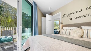 Een slaapkamer met een groot bed en uitzicht op de natuur, met een muur waarop staat 'Happiness in waves'.