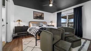 Ein modernes Schlafzimmer mit einem Bett, zwei Nachttischen, einem Deckenventilator und Blick durch ein großes Fenster.