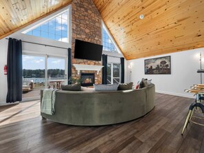 A spacious living room with a stone fireplace, a large window, and a view of the outdoors. - Lakefront Retreat in Sand Lake (Sand Lake)