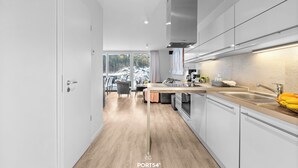 A modern kitchen with white cabinetry, a wooden countertop, and a large window providing a view of the outdoors. - Modern beachfront holiday apartment with luxury amenities on Priwall Travemünde (Lübeck)