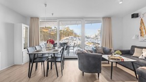 A modern living room with a dining area, large windows, and a view of a snowy landscape. - Modern beachfront holiday apartment with luxury amenities on Priwall Travemünde (Lübeck)