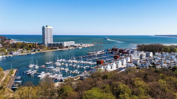A marina with boats, a tall building, and residential buildings. - Modern beachfront holiday apartment with luxury amenities on Priwall Travemünde (Lübeck)