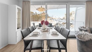 A modern dining room with a large table, black chairs, and a view of a snowy landscape through large windows. - Modern beachfront holiday apartment with luxury amenities on Priwall Travemünde (Lübeck)