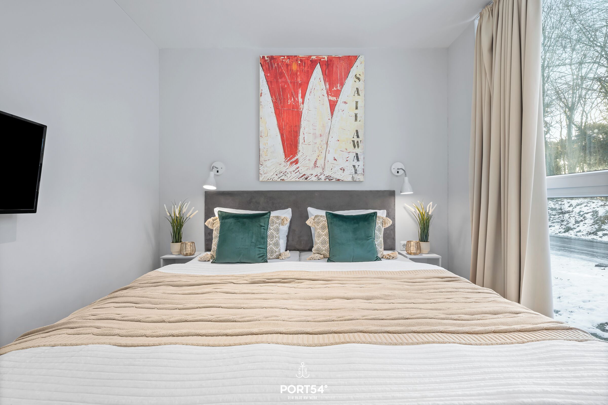 Un dormitorio moderno con una cama grande, un televisor montado y un cuadro de veleros.
