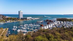 A marina with numerous boats docked, a tall building in the background, and a coastal landscape. - Bright Family Apartment with Covered Balcony and Wellness near Priwall Beach (Lübeck)