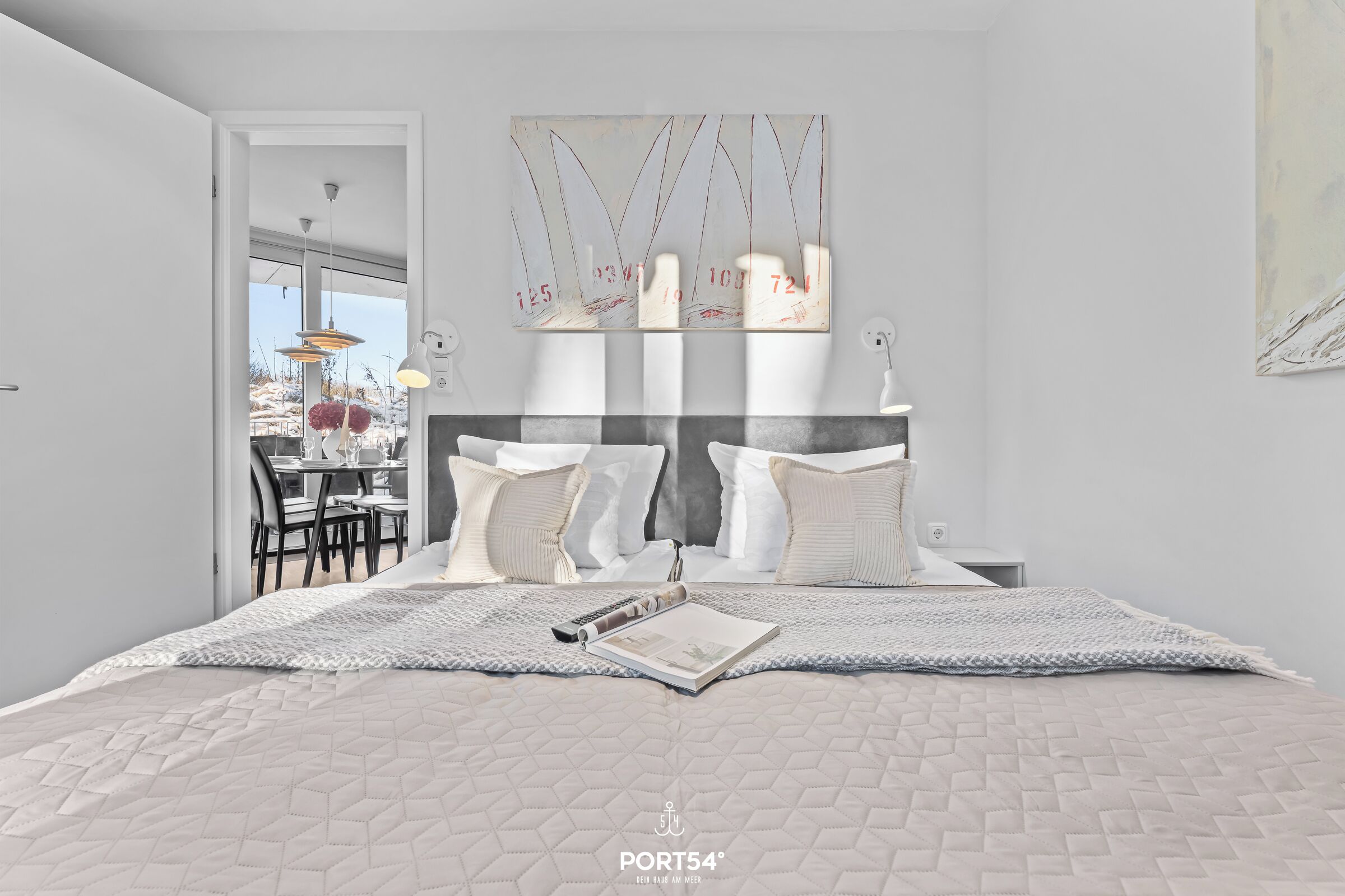 Ein modernes Schlafzimmer mit einem großen Bett, einem Kopfteil mit Zahlen, einem Essbereich, der durch eine offene Tür sichtbar ist, und Blick auf eine verschneite Landschaft.