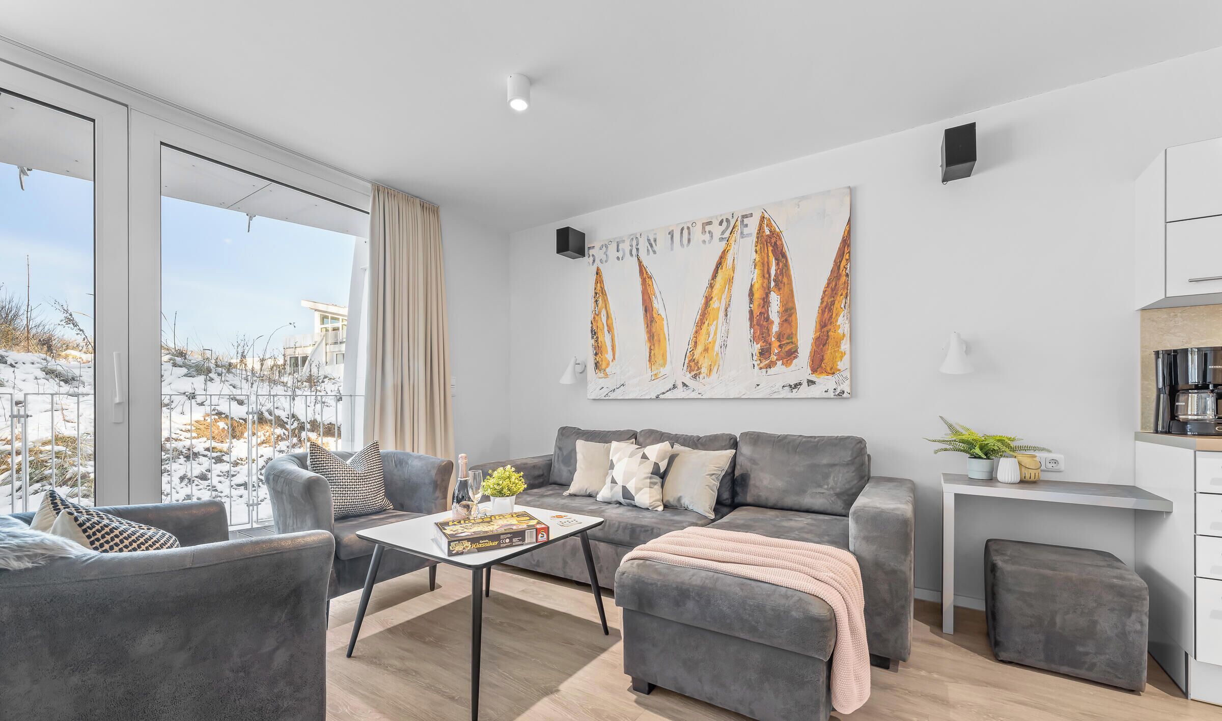 Ein modernes Wohnzimmer mit einem grauen Sofa, einem Couchtisch und einem Gemälde von Segelbooten.
