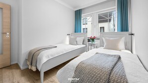Una habitación de hotel con dos camas, una puerta de madera y una ventana con cortinas azules.