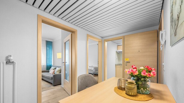 Una habitación de hotel moderna con una mesa de comedor de madera, un jarrón de flores y vistas al salón.